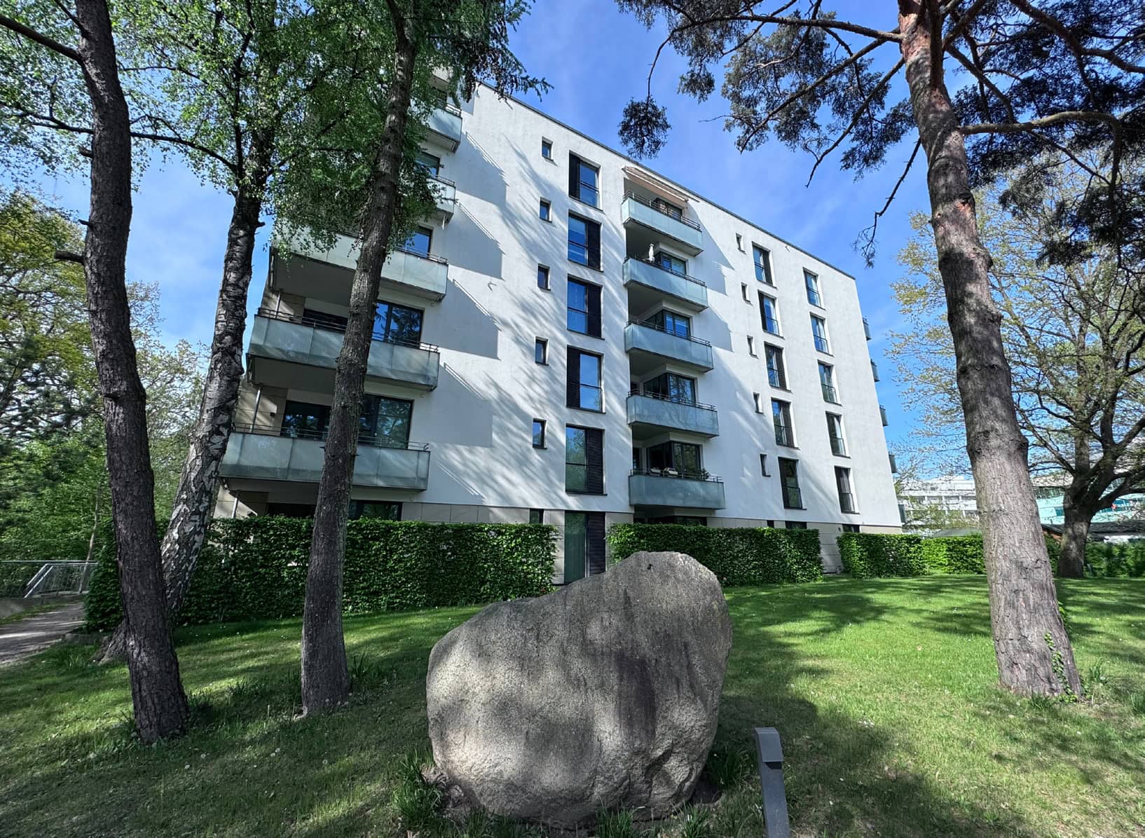 Das Bild zeigt den Forum Alstertal Neubau aus 2014 in der Totalen hinter Bäumen im Grünen während eines herrlichen Frühlingstages